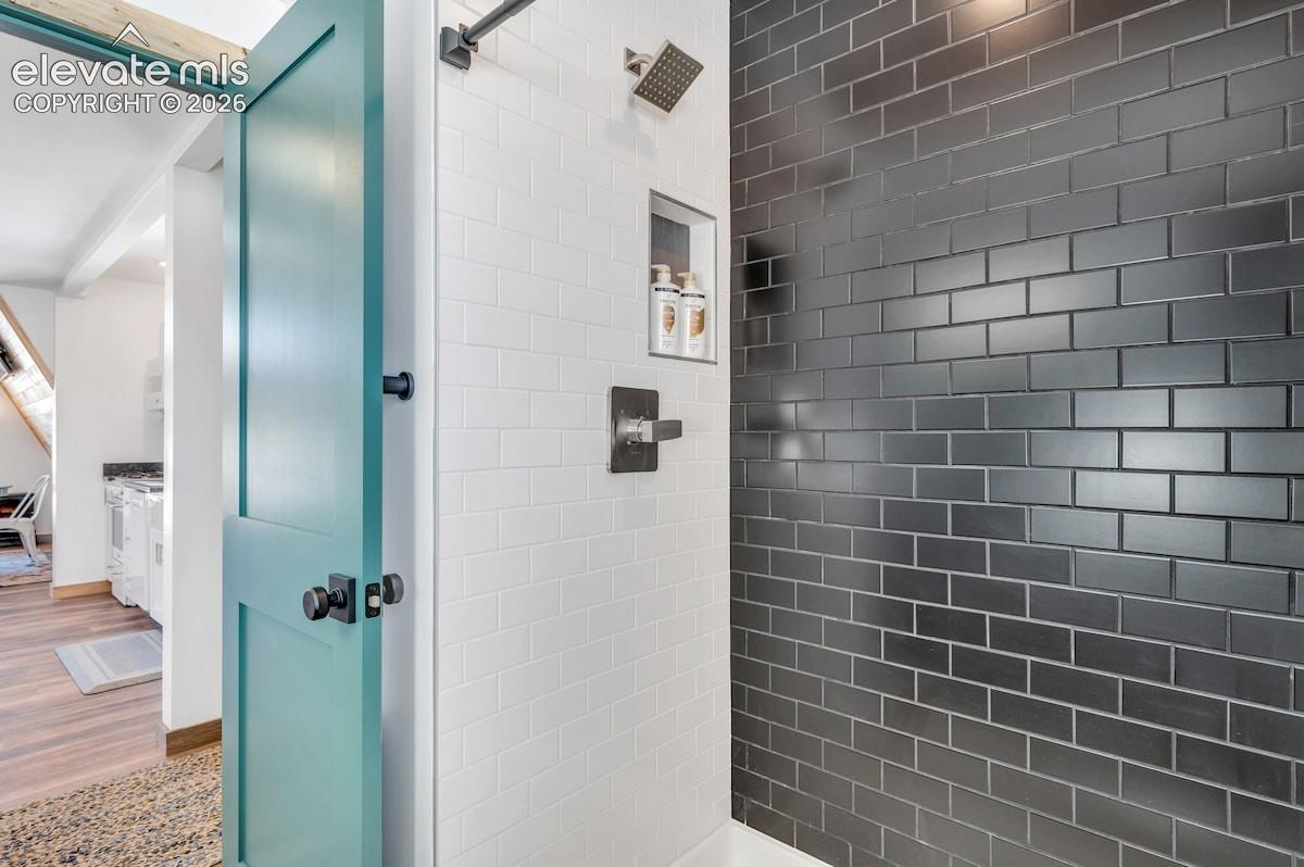 Shower enclosure featuring matte black subway tile, white subway tile wall accents, a built-in recessed niche, rainfall shower head, and a single-handle faucet