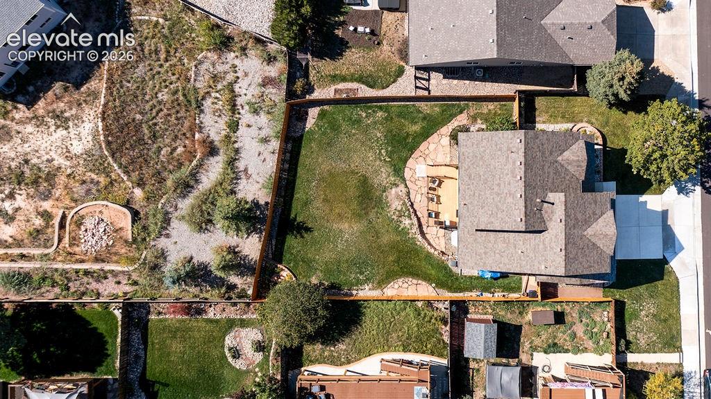 Aerial perspective of property featuring a fenced backyard, lawn space, stone hardscaping, and a concrete driveway