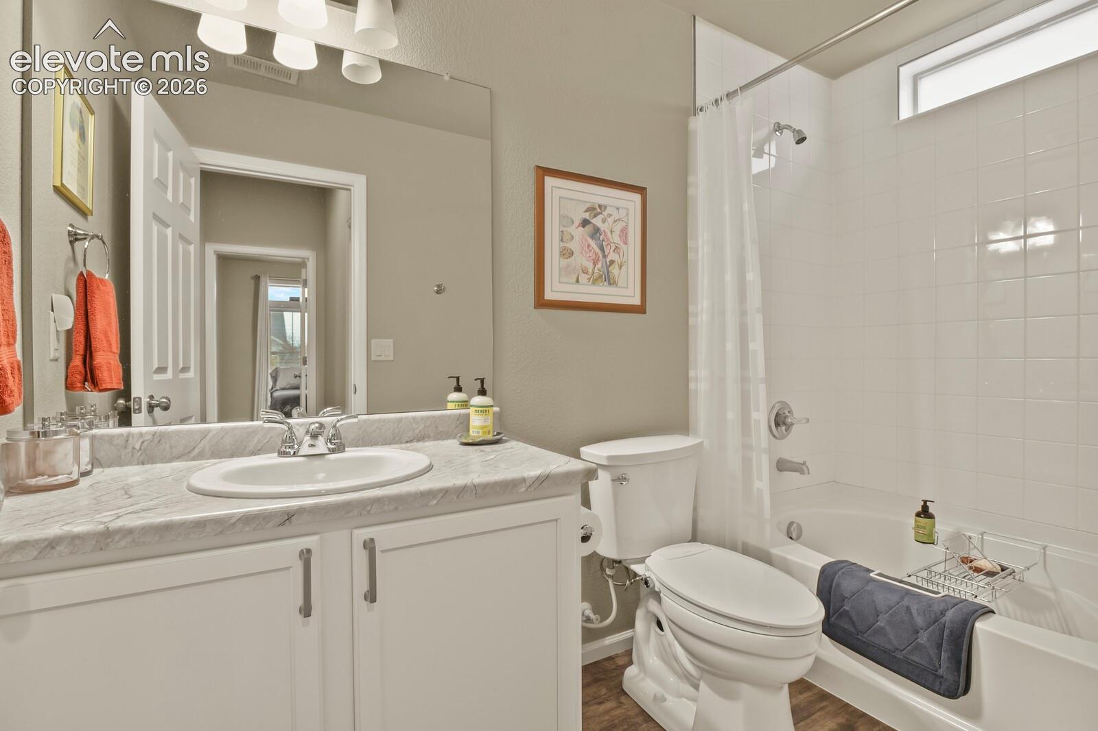 Bathroom featuring a vanity with an oval undermount sink, stone-finish countertop, white cabinetry, large wall-mounted mirror with light fixture, and a tiled shower-tub combination, toilet/bidet with a clerestory window