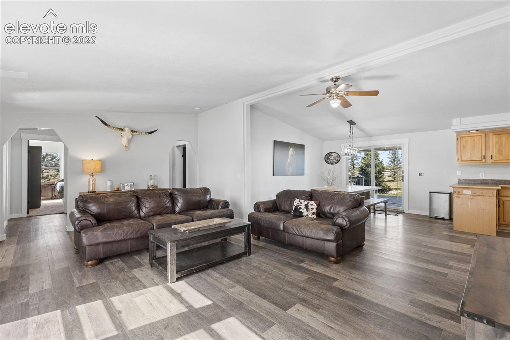 Open-concept interior featuring wood-finish flooring, vaulted ceilings with a mounted paddle fan, and sliding glass doors with exterior access