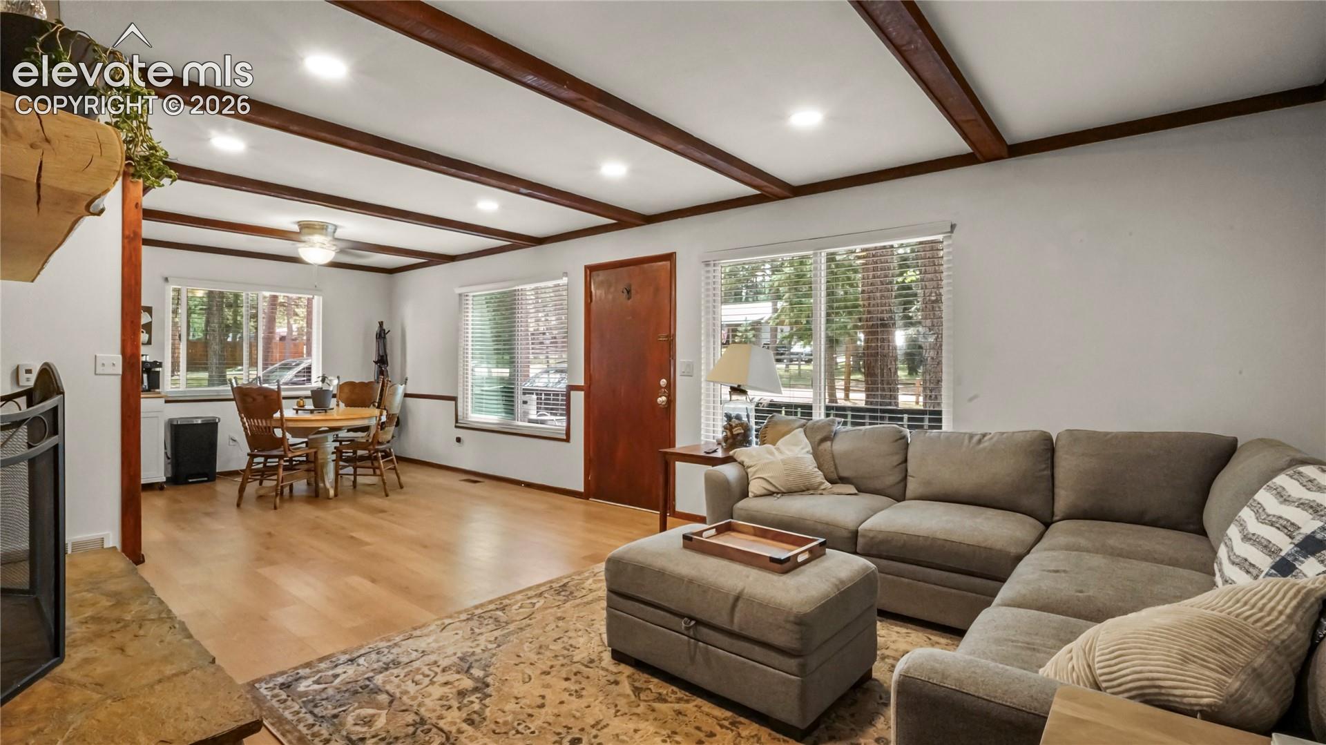Exposed wood beam ceiling, recessed lighting, LVP flooring, multiple windows, and a built-in mantel