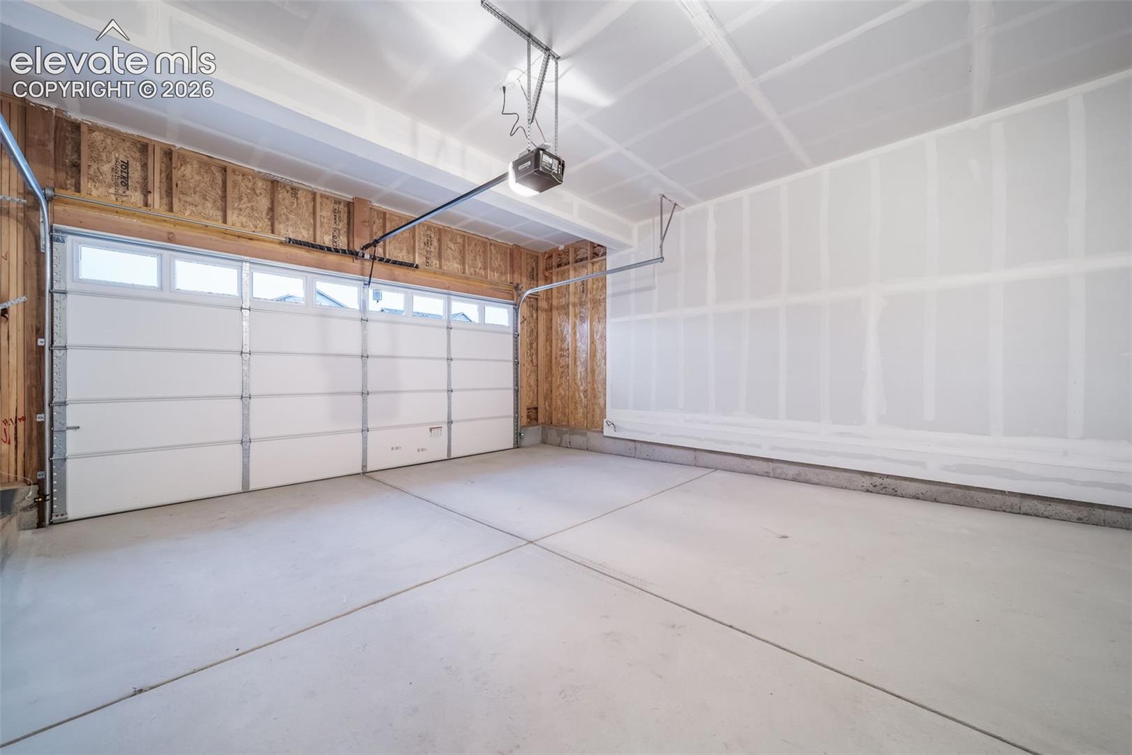 Concrete slab flooring, white paneled garage door with windows, exposed wood framing, drywall-finished wall, and an automatic garage door opener
*photos of a model home*
