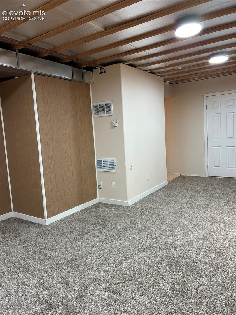 Neutral-toned carpeting, wood-paneled walls, exposed joist ceiling, and a six-panel interior door