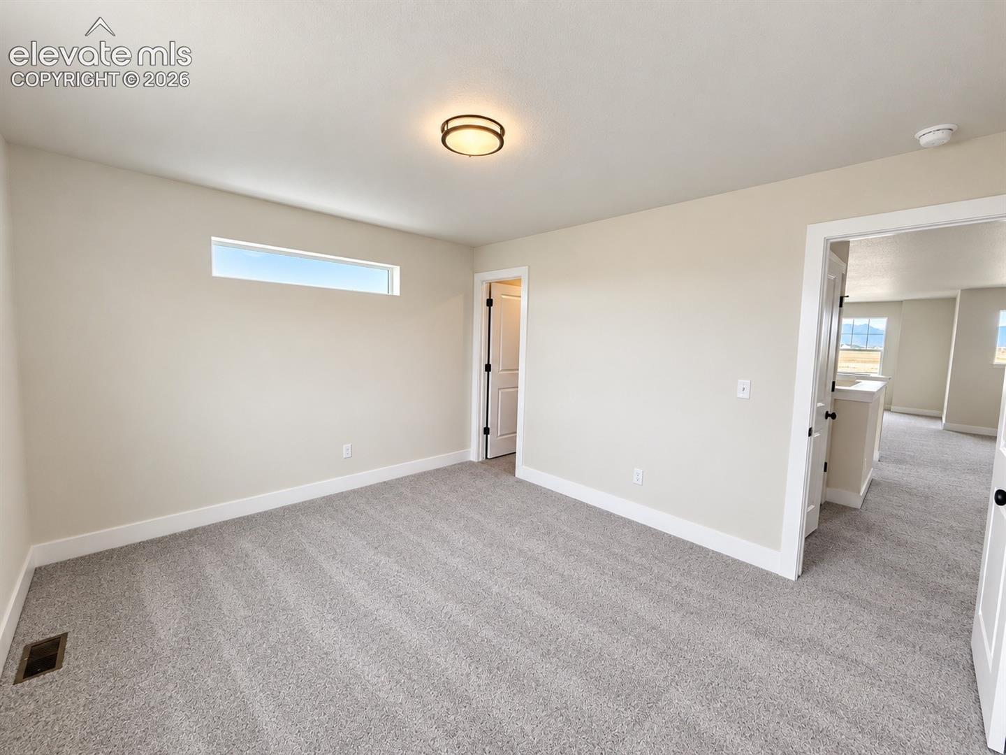 Neutral wall tones paired with neutral carpeting, a horizontal clerestory window, and a circular flush-mount overhead light fixture