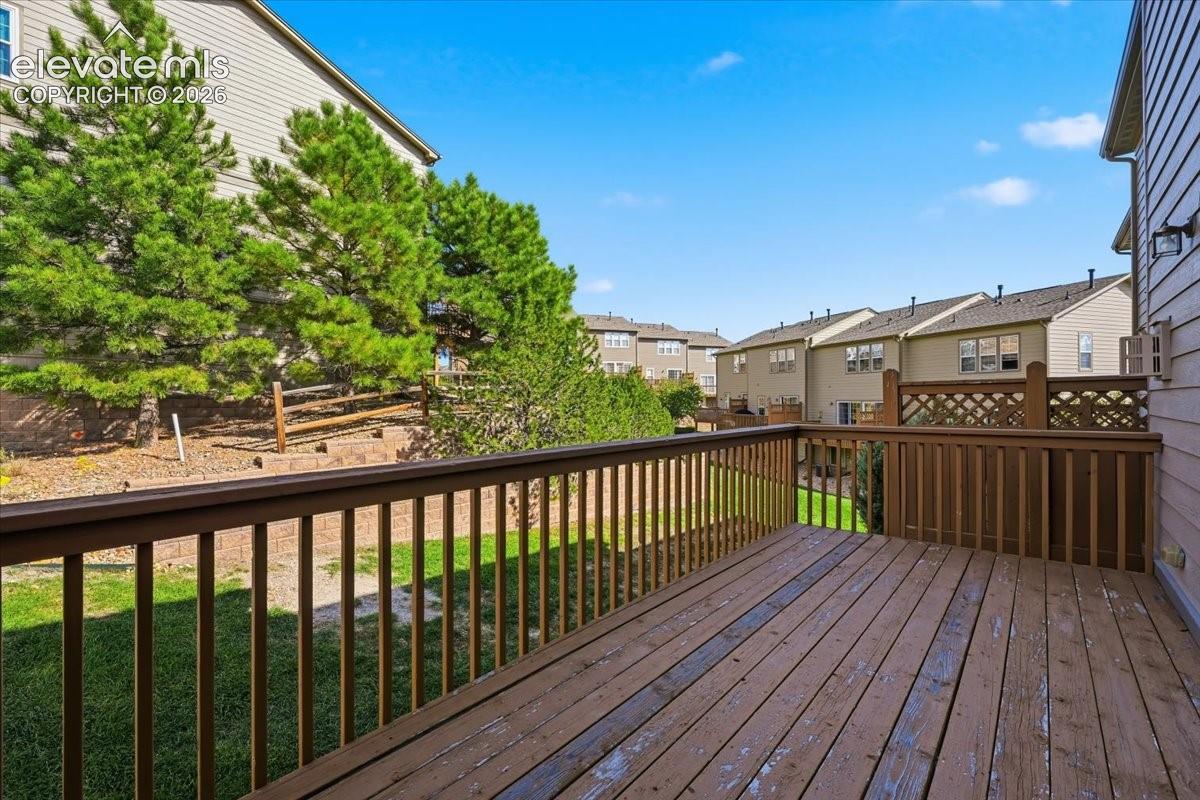 Expansive wooden deck with a lattice privacy panel, surrounded by mature evergreen trees and a sloped, landscaped yard