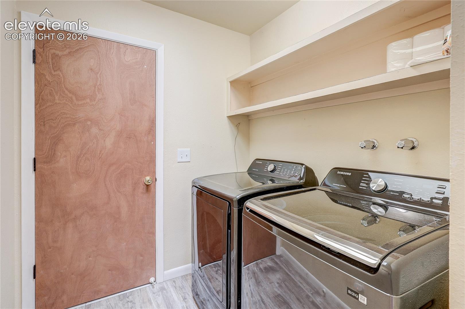 Laundry space featuring wood-finish flooring, a flat-panel interior door, and built-in upper shelving