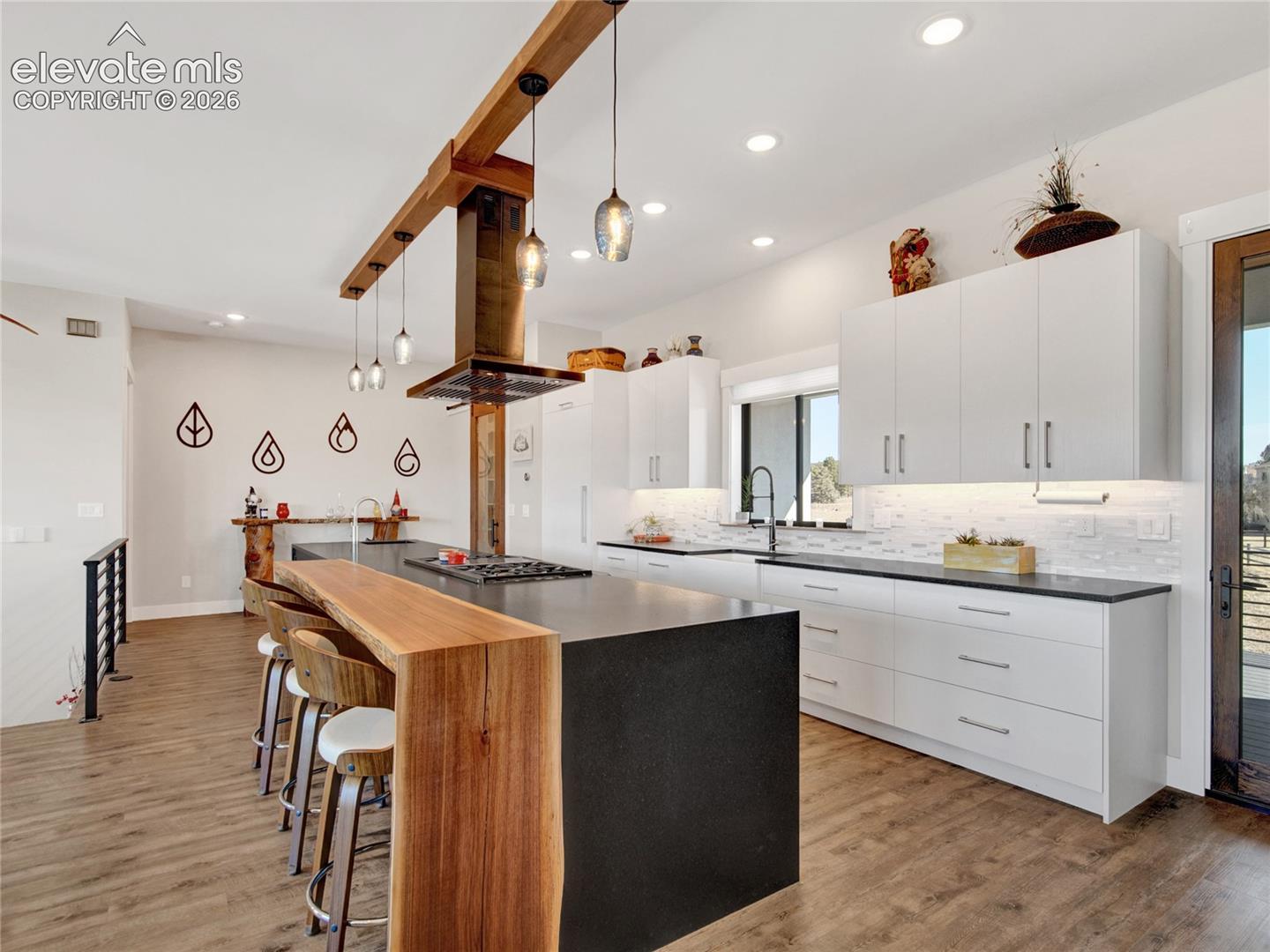 Modern kitchen featuring a large island with a live-edge wood breakfast bar, a built-in range, and a wood beam ceiling accent with pendant lighting