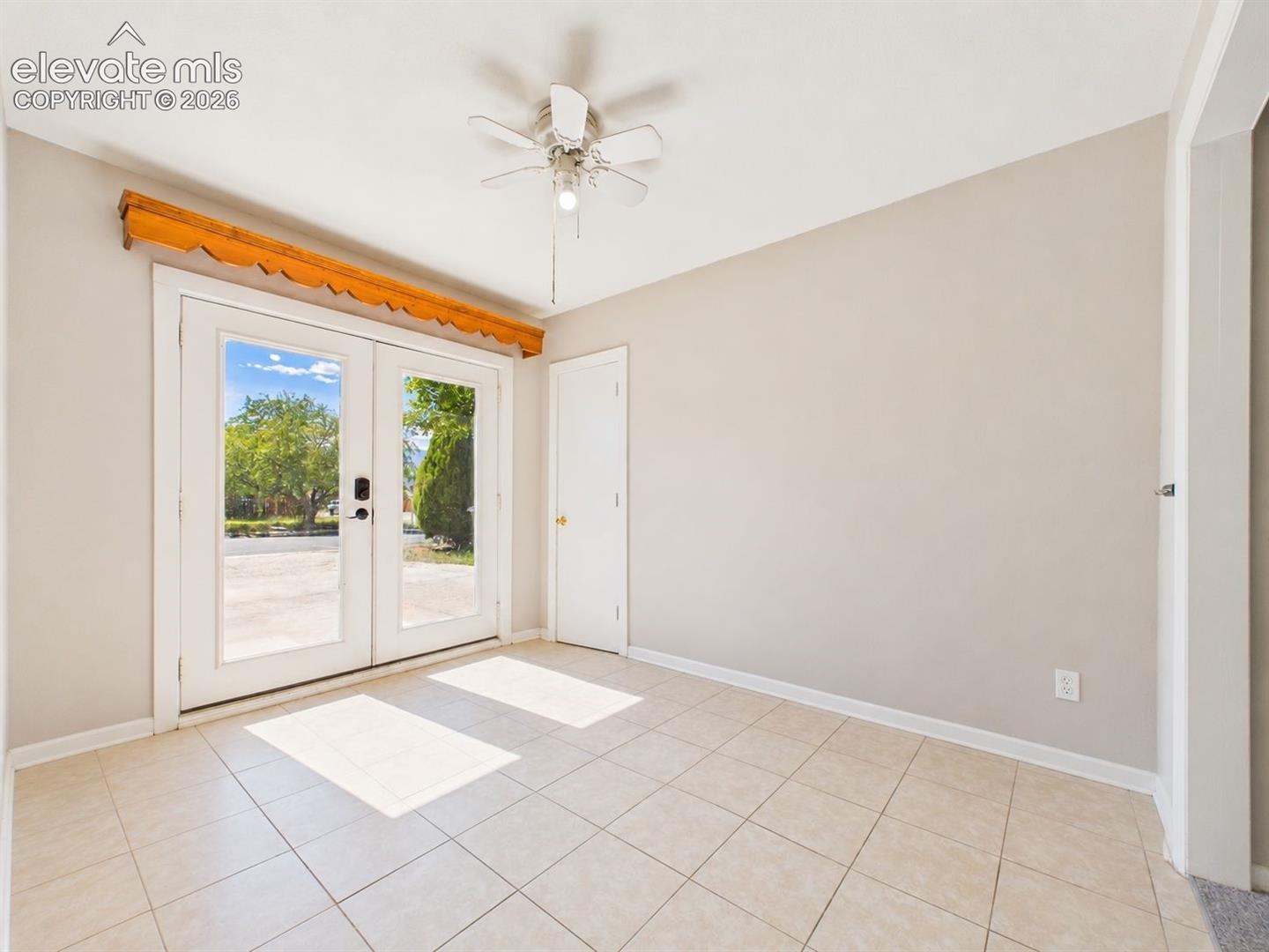 Glass-paneled double doors bring abundant natural light into this tiled entry area, complemented by neutral finishes and a ceiling fan.