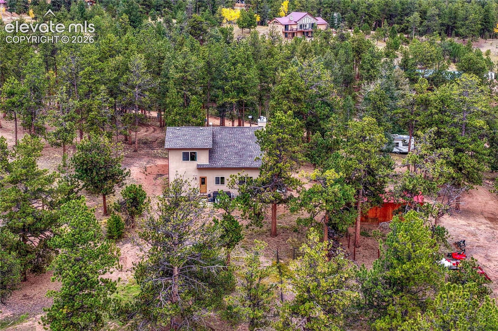 Residence featuring a shingled roof, neutral-toned stucco exterior, and placement within a forested lot with mature coniferous trees