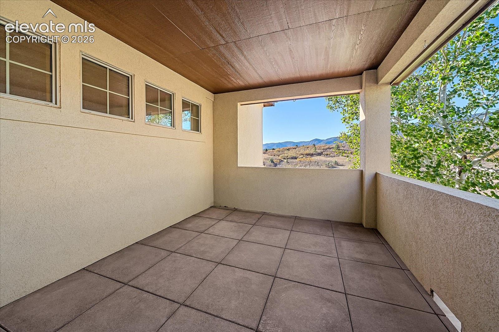 Covered balcony featuring square tile flooring, a wood-finished ceiling, stucco walls, and mountain scenery