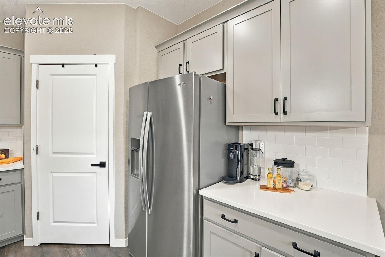 Shaker-style cabinetry with matte black hardware, stainless steel refrigerator, white quartz countertops, and white subway tile backsplash