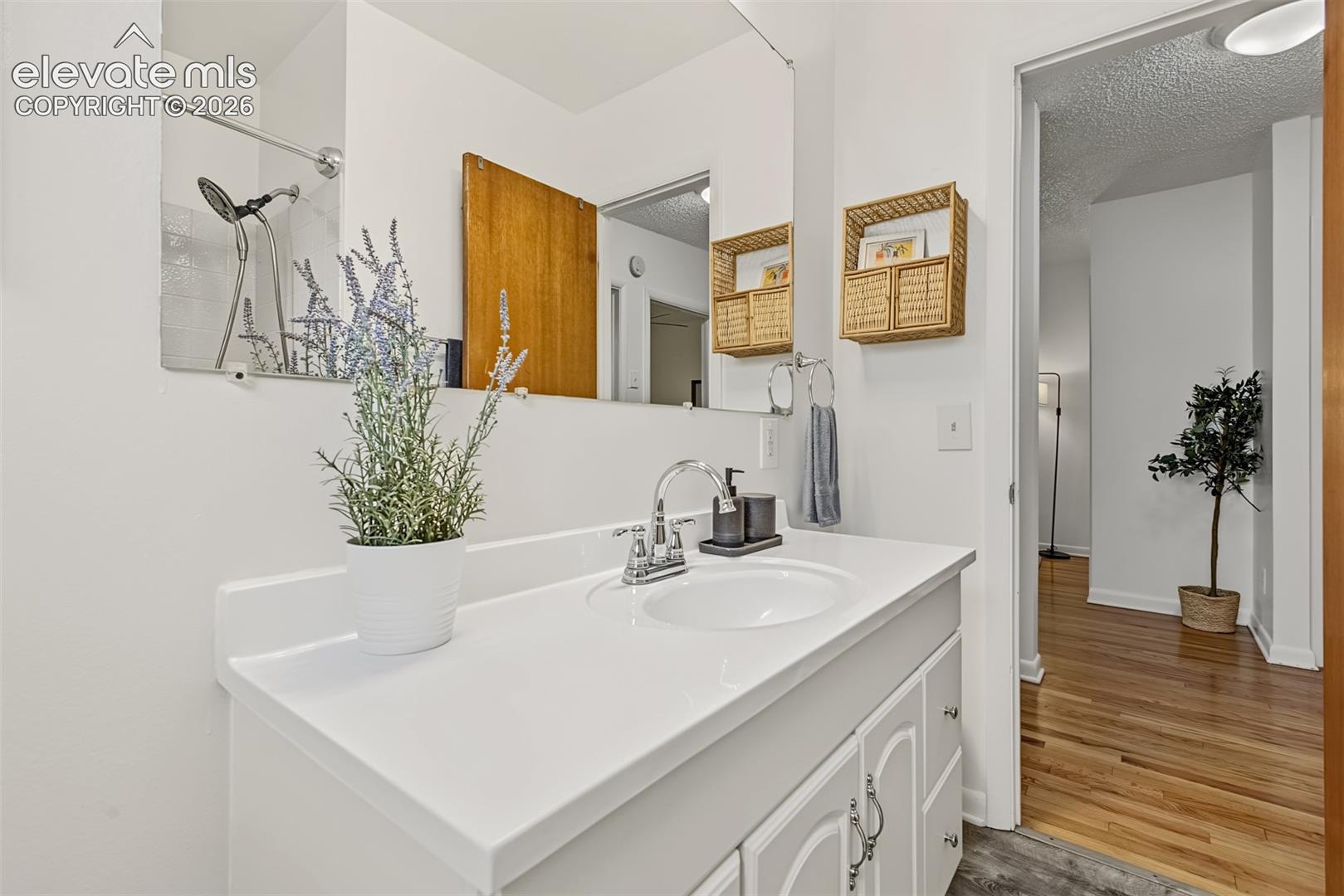 Bathroom vanity featuring a white countertop with an integrated oval sink, chrome finish faucet, white cabinetry with decorative hardware, and a wall-to-wall vanity mirror