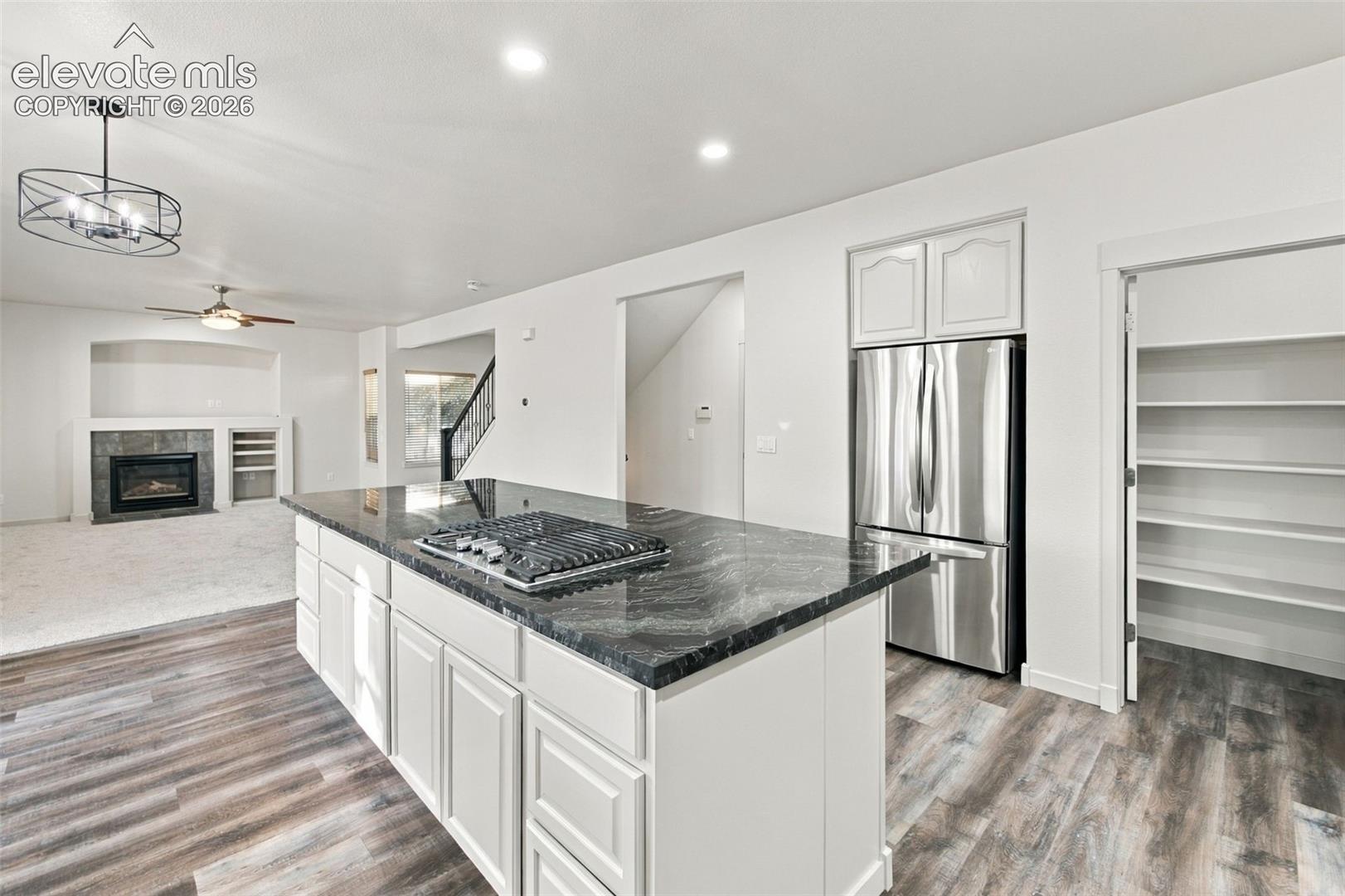 Kitchen island with a dark stone countertop and integrated gas cooktop, white cabinetry, stainless steel refrigerator, and walk-in pantry