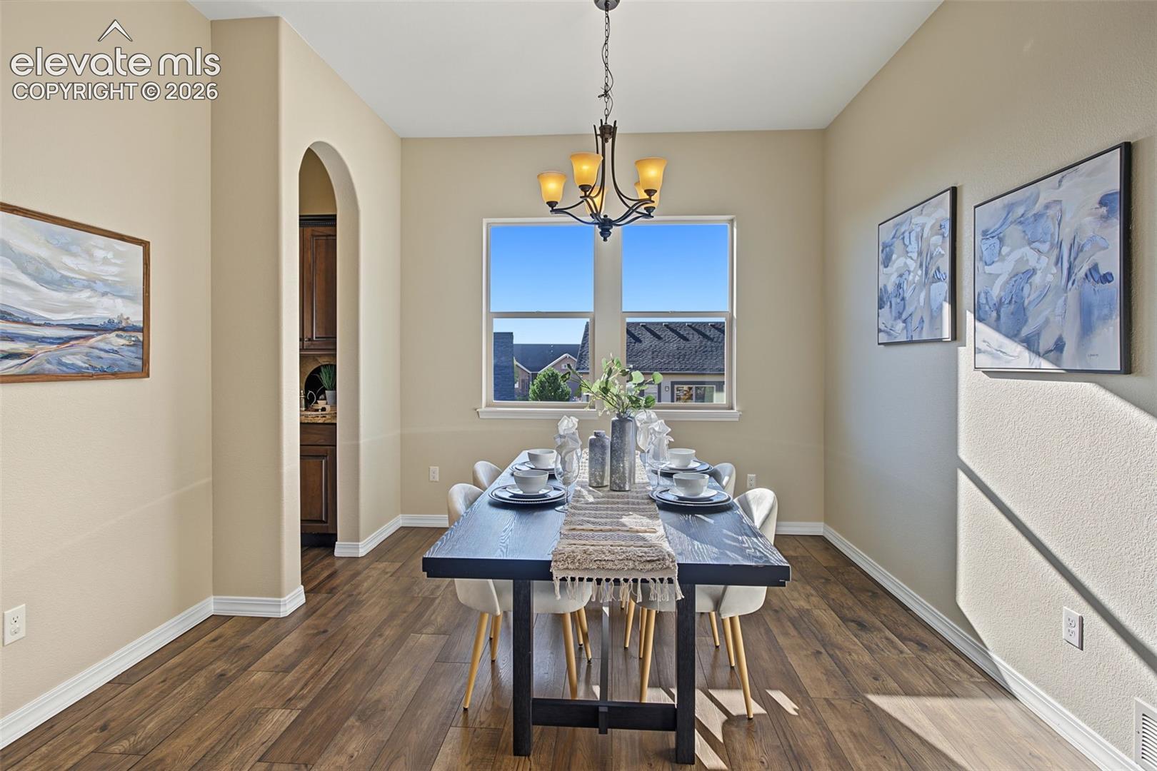 Dining area featuring wood-finish flooring, a decorative arched entryway, a large dual-pane window, and a multi-arm metal chandelier