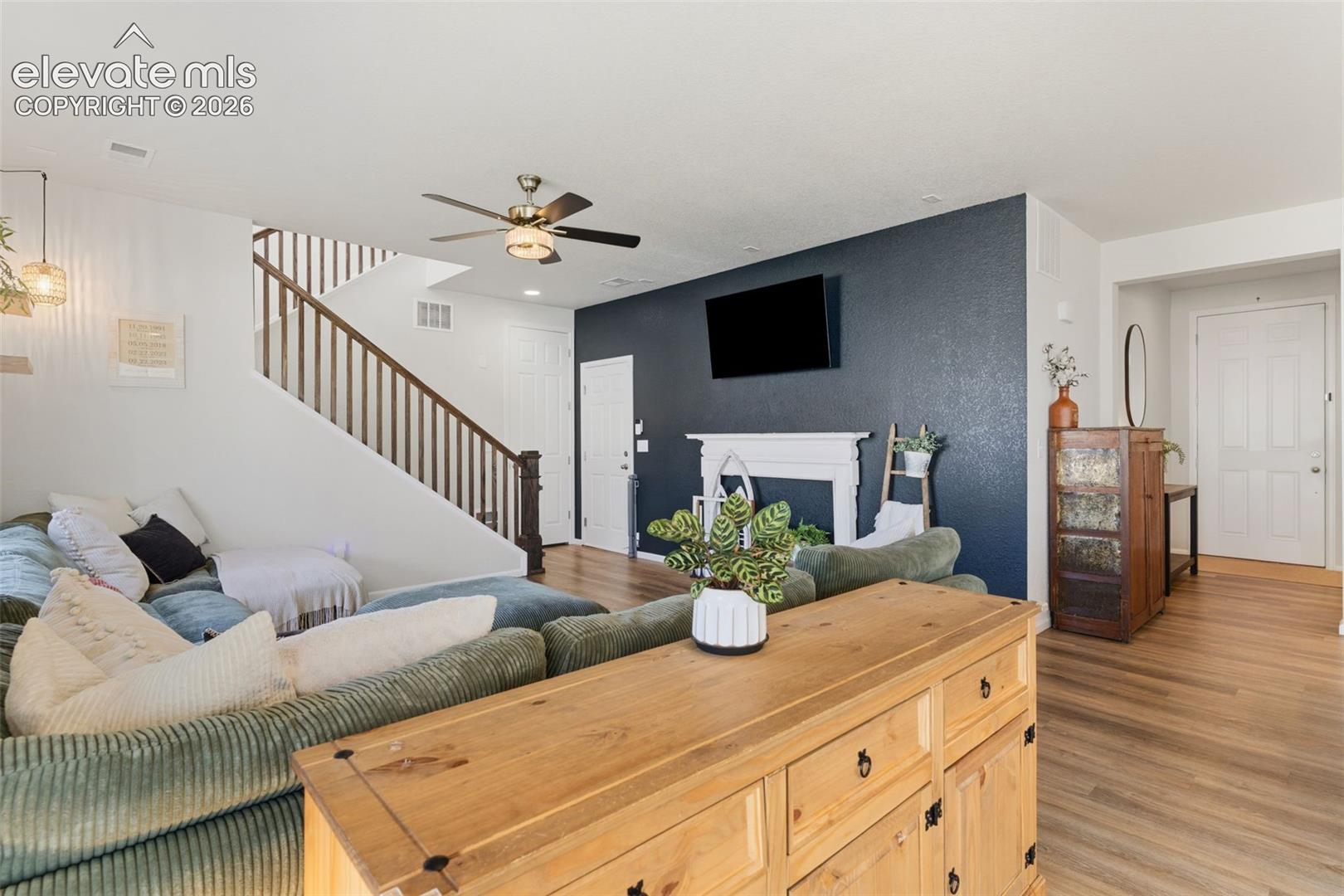 Living area featuring wood-finish flooring, a white mantelpiece, and a contrasting accent wall