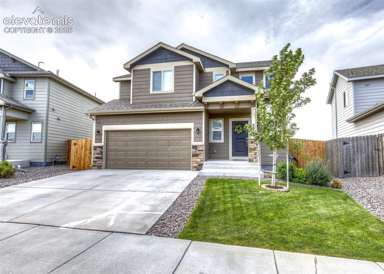 Two-story exterior featuring horizontal lap siding, stone veneer accents, multi-gabled rooflines, attached two-car garage, and concrete driveway