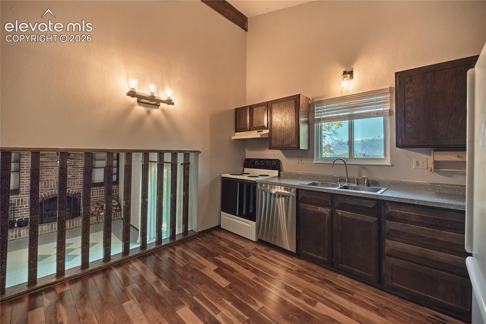Kitchen featuring dark wood cabinetry, stainless steel appliances, wood-finish flooring, high vaulted ceilings, and decorative interior railing