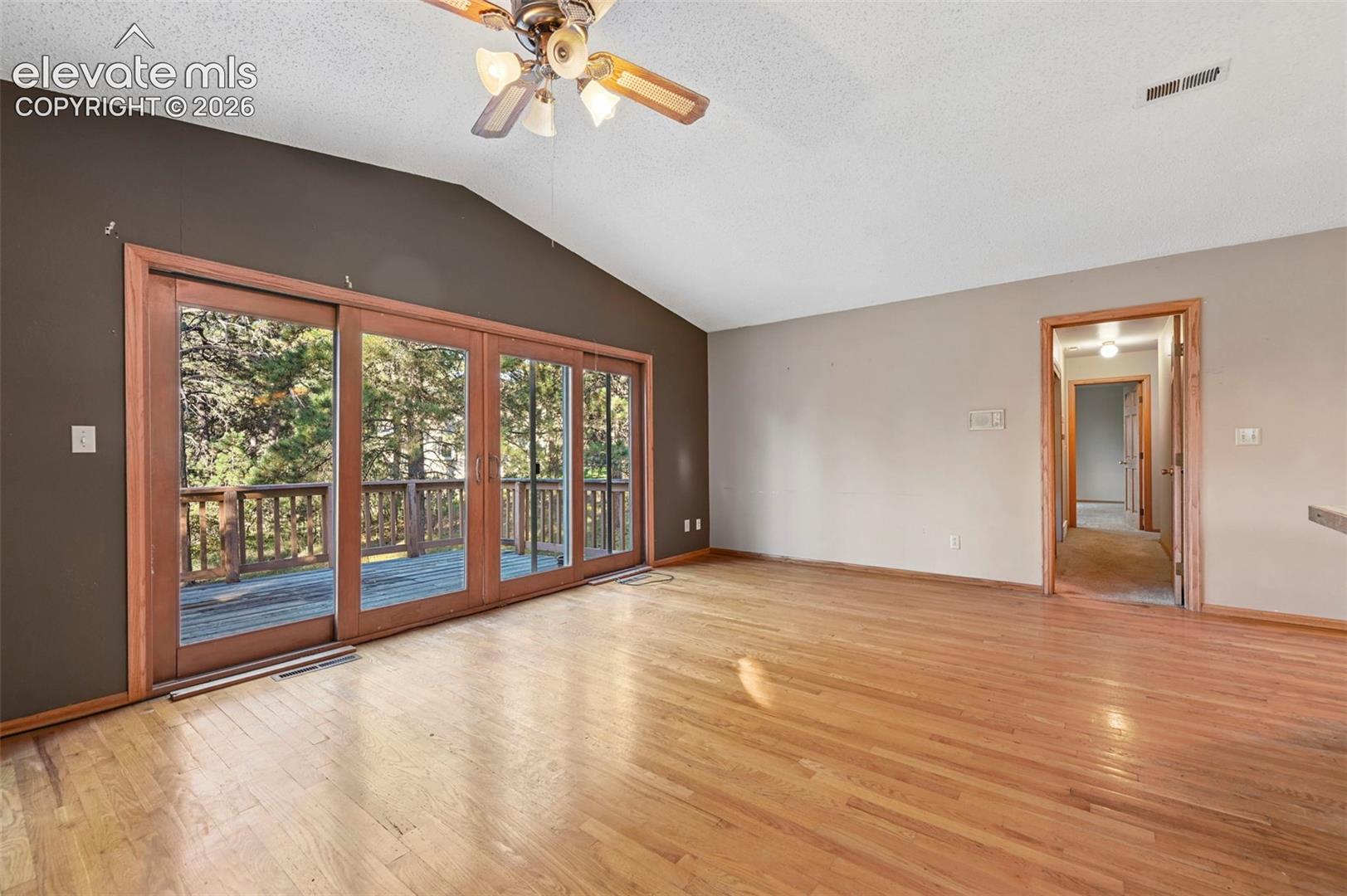 Vaulted ceiling with a ceiling fan, wood-finish flooring, and sliding glass doors leading to a wooden deck with railing