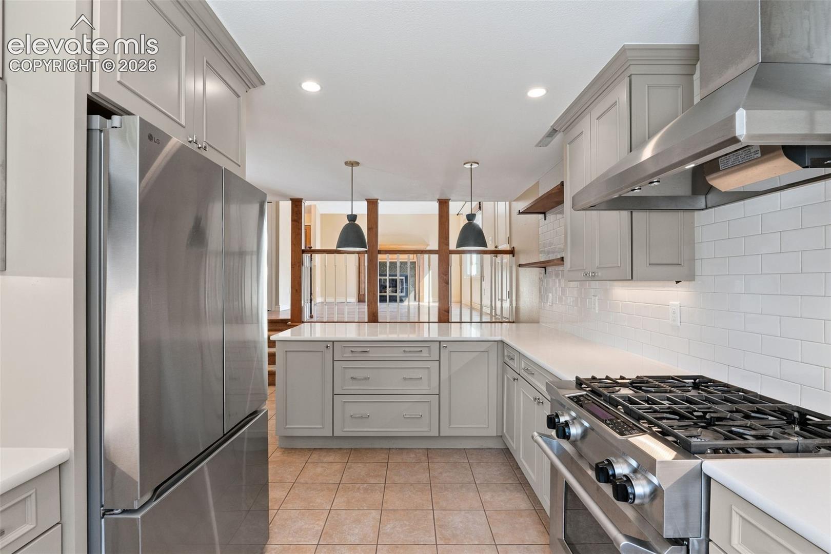 Kitchen featuring light gray shaker-style cabinetry, white quartz countertops, subway tile backsplash, stainless steel professional-grade range with matching hood, and recessed lighting