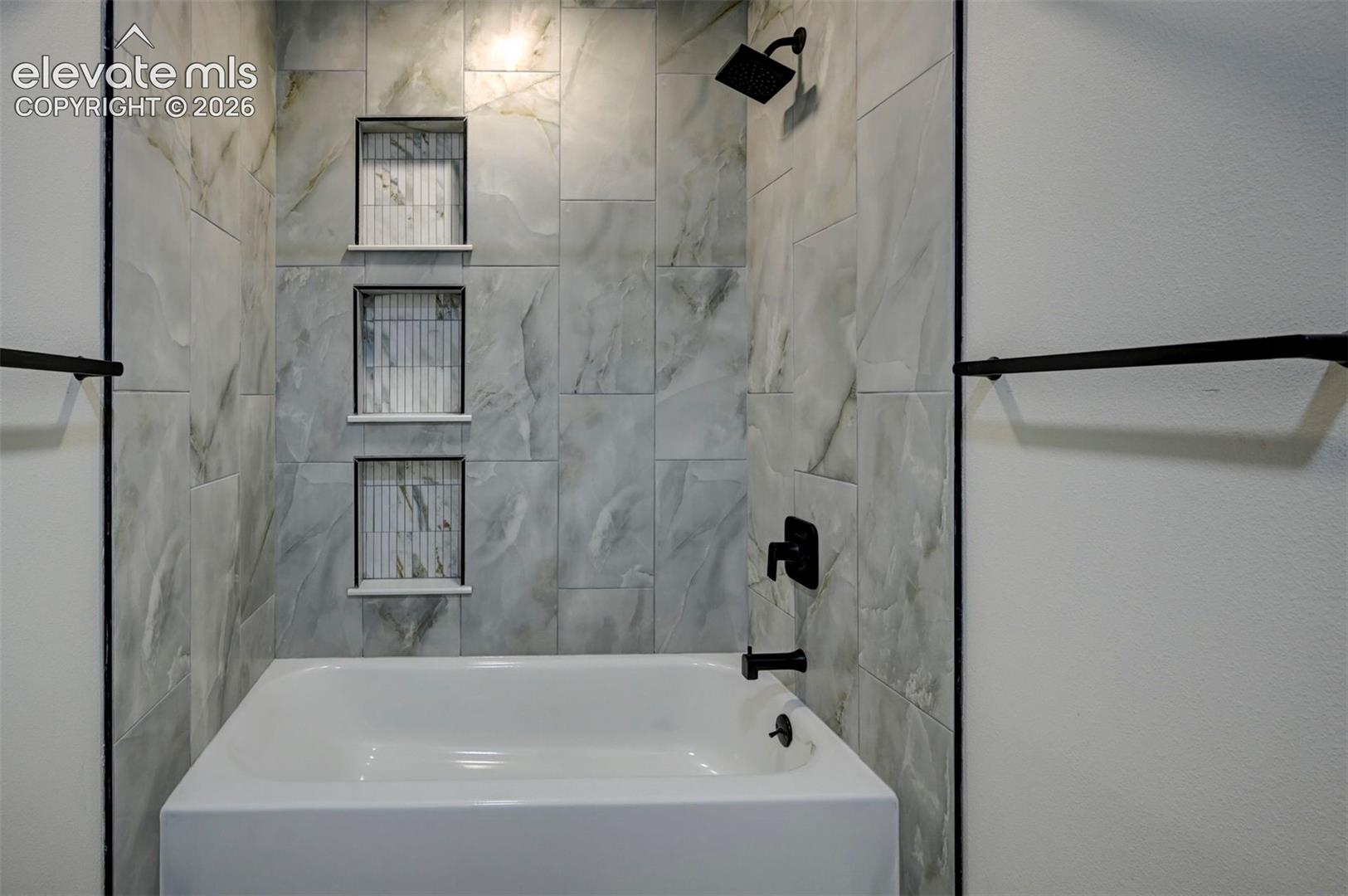 Bathtub with large-format tile surround, three built-in wall niches featuring vertical accent tile, and matte black plumbing fixtures