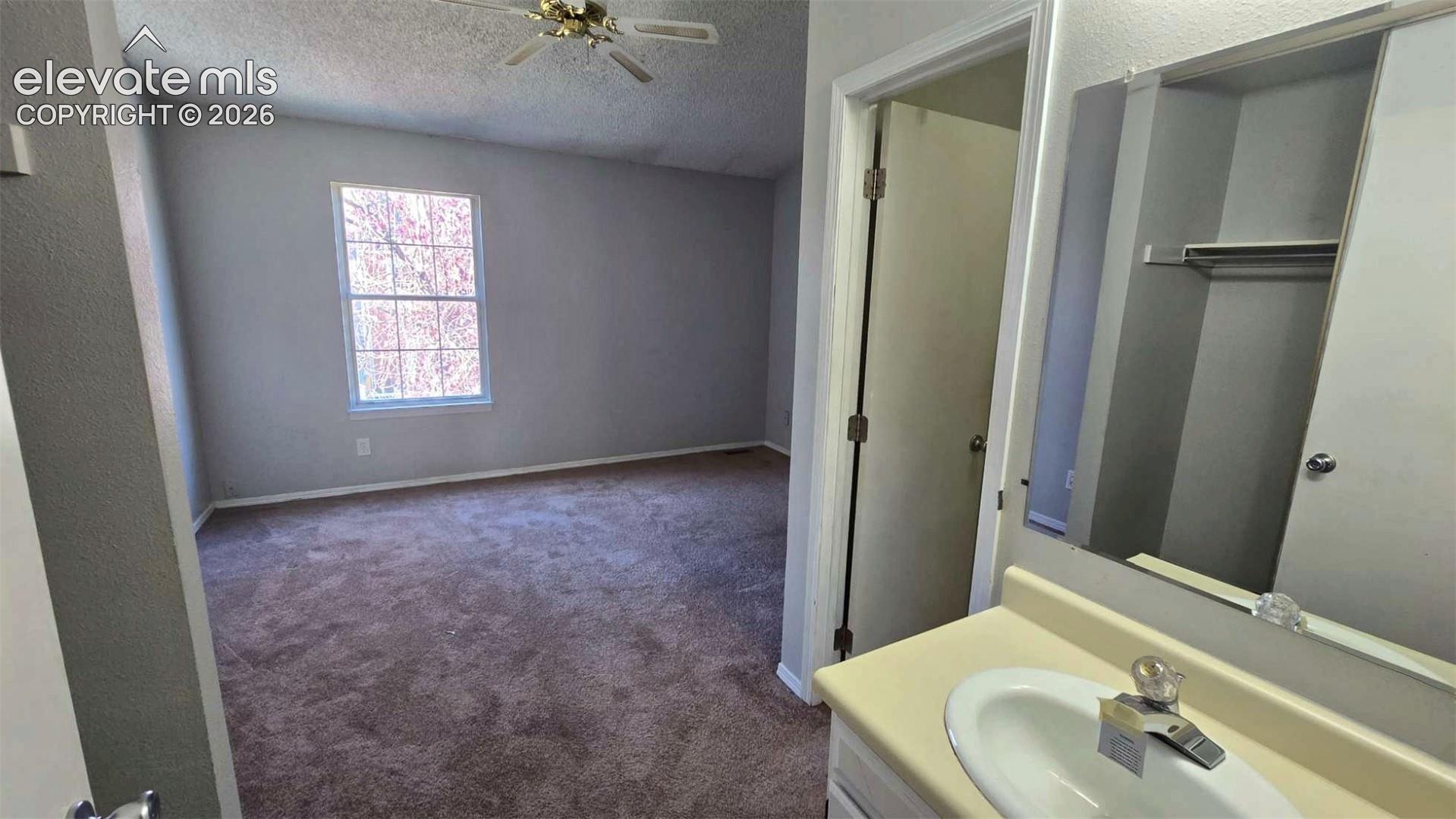 Interior space featuring neutral-toned walls, carpeting, a ceiling fan, a multi-pane window, and a built-in vanity with a sink and mirror