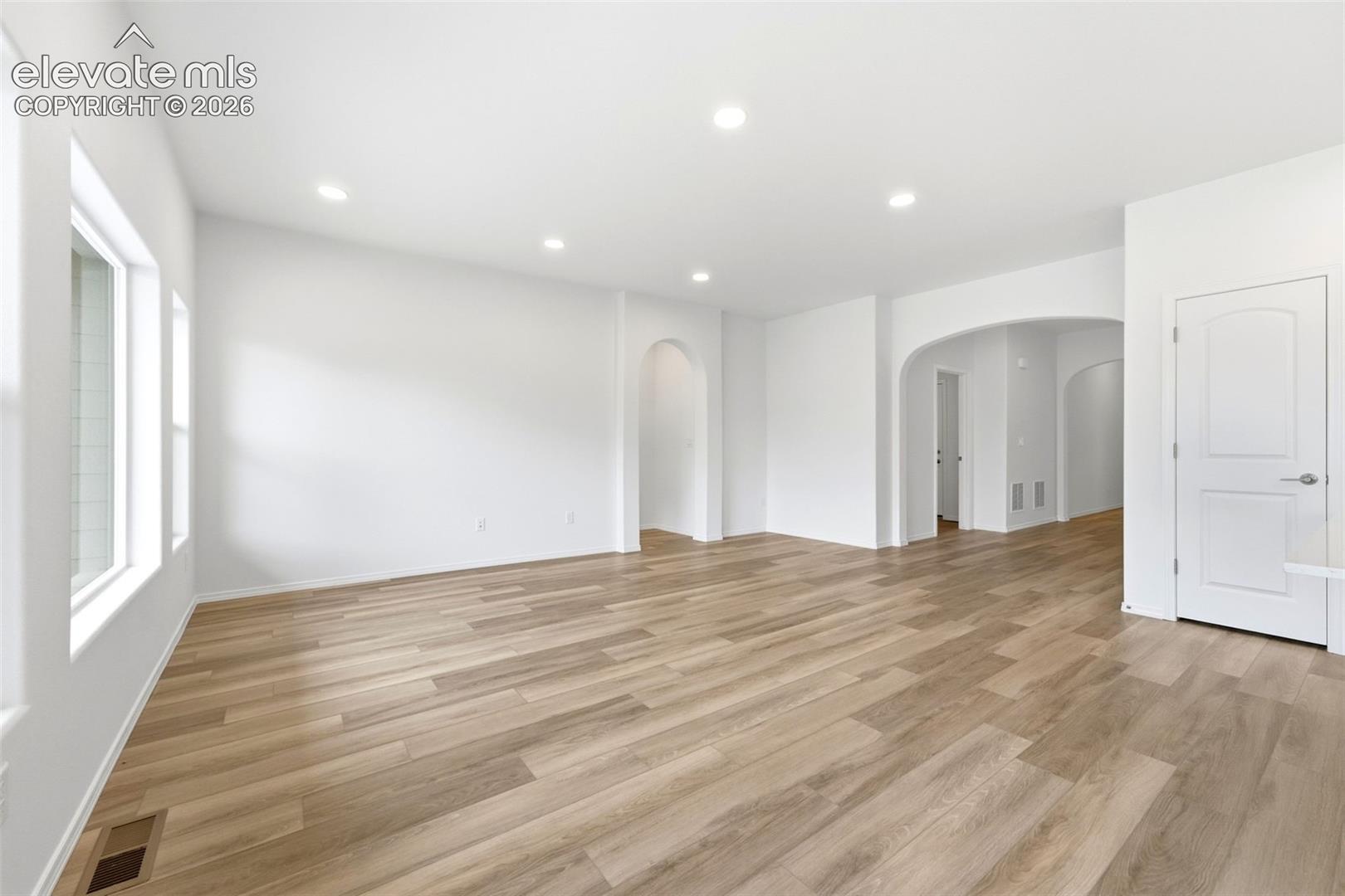 Open-concept interior featuring wood-finish flooring, recessed lighting, and arched architectural doorways