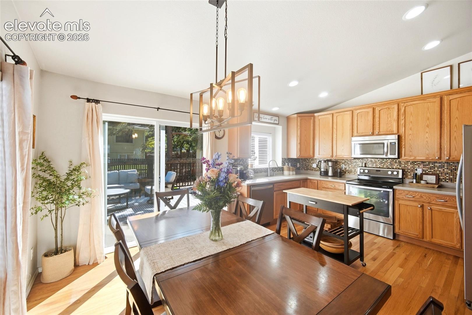 Wood-finish flooring throughout, kitchen with wood cabinetry and stainless steel appliances, sliding glass door leading to an outdoor deck, recessed lighting, and a contemporary chandelier