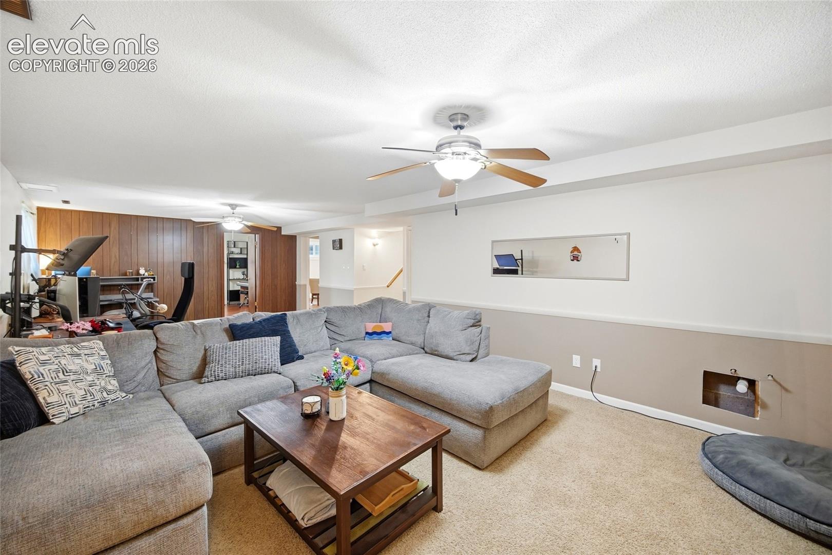 Neutral-tone wall finishes with chair rail, wood-panel accent wall, dual ceiling fans, and wall-to-wall carpeting