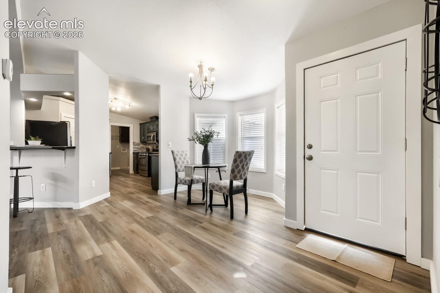 Wood-finish flooring, bay windows with blinds, multi-panel exterior entry door, and multi-arm chandelier lighting fixture
