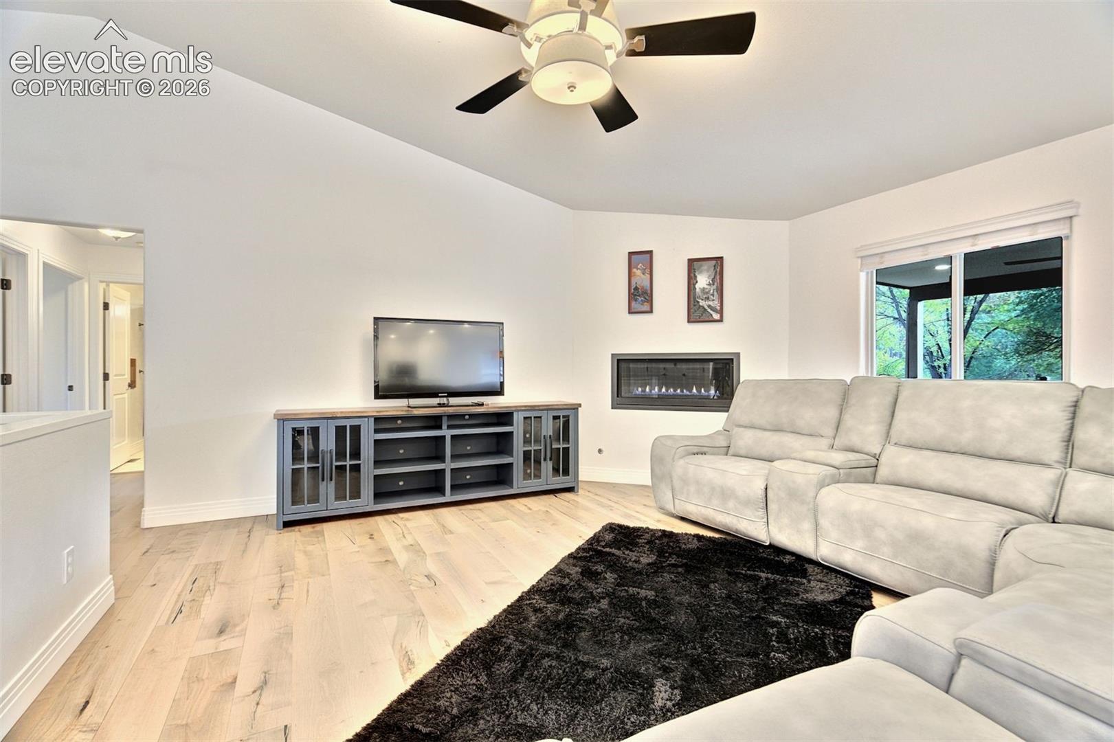 Vaulted ceilings, wood-finish flooring, linear wall-mounted fireplace, and ceiling fan with integrated lighting