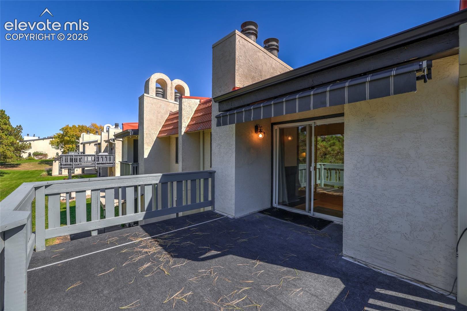 Stucco exterior balcony featuring a retractable awning, painted wood railing, sliding glass door, and exterior wall-mounted light fixture