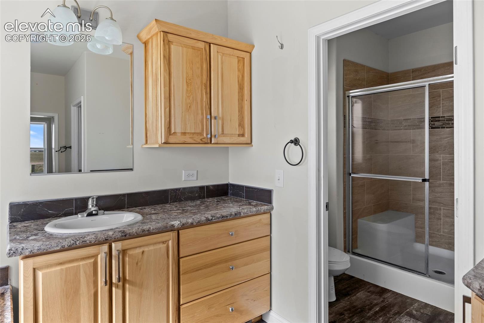 Natural wood-finish cabinetry, solid surface countertop with integrated sink, three-light vanity fixture, and tiled shower enclosure with built-in bench