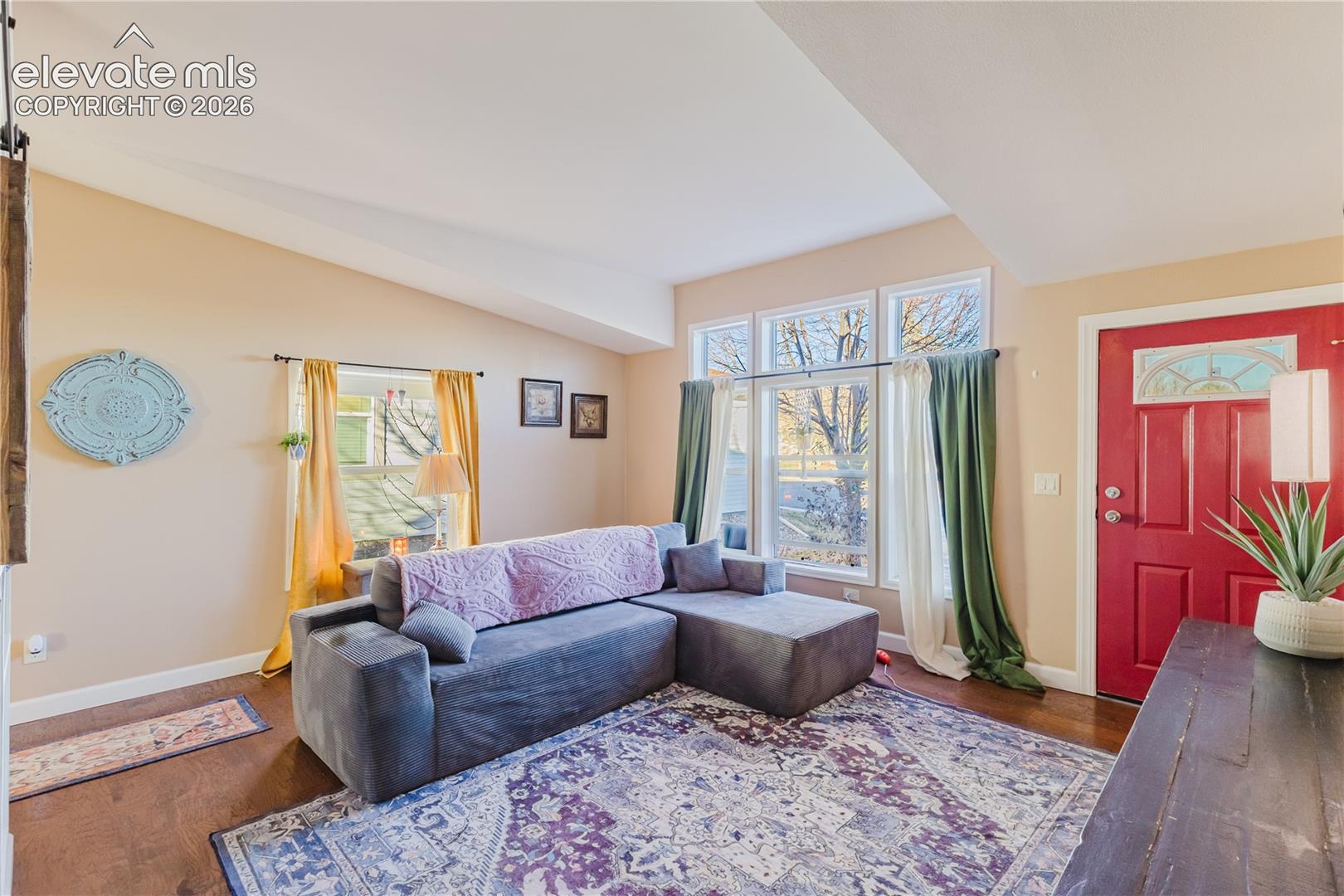 Vaulted ceiling, wood-finish flooring, red entry door with decorative glass, and multiple windows