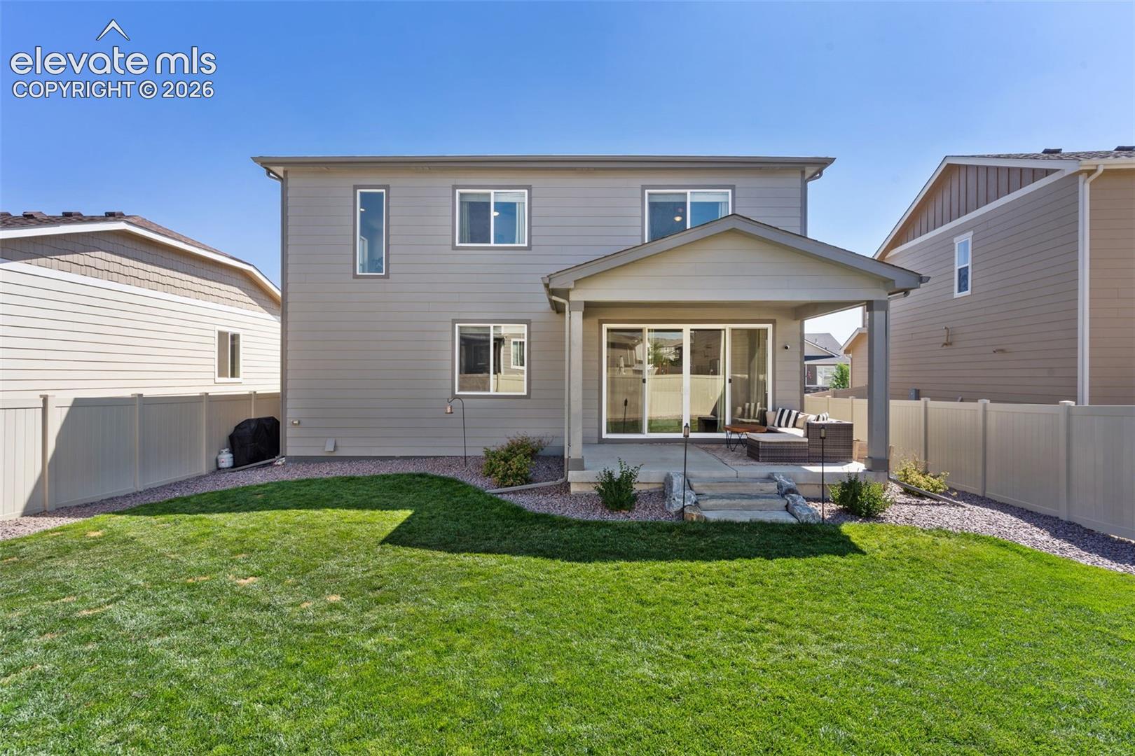 Spacious backyard with a covered patio, multiple windows on the rear facade, and full vinyl fencing