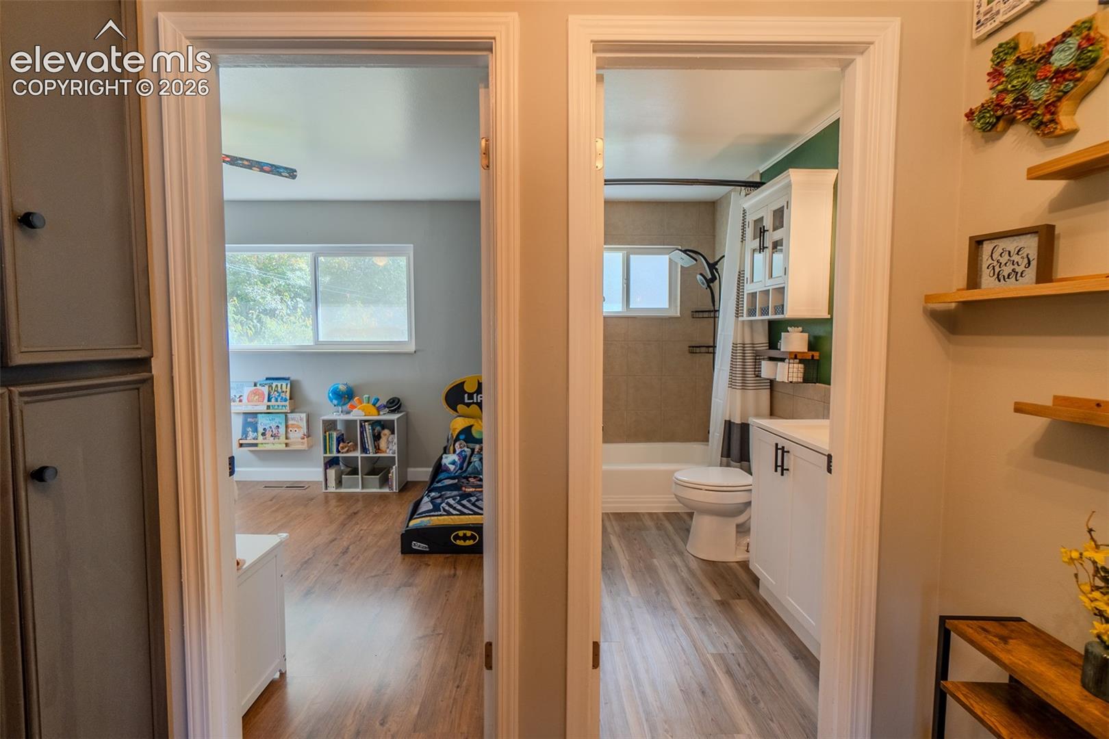 Two separate doorways featuring white door casings, wood-finish flooring, and a bathroom equipped with a white vanity cabinet and a wall-mounted medicine cabinet