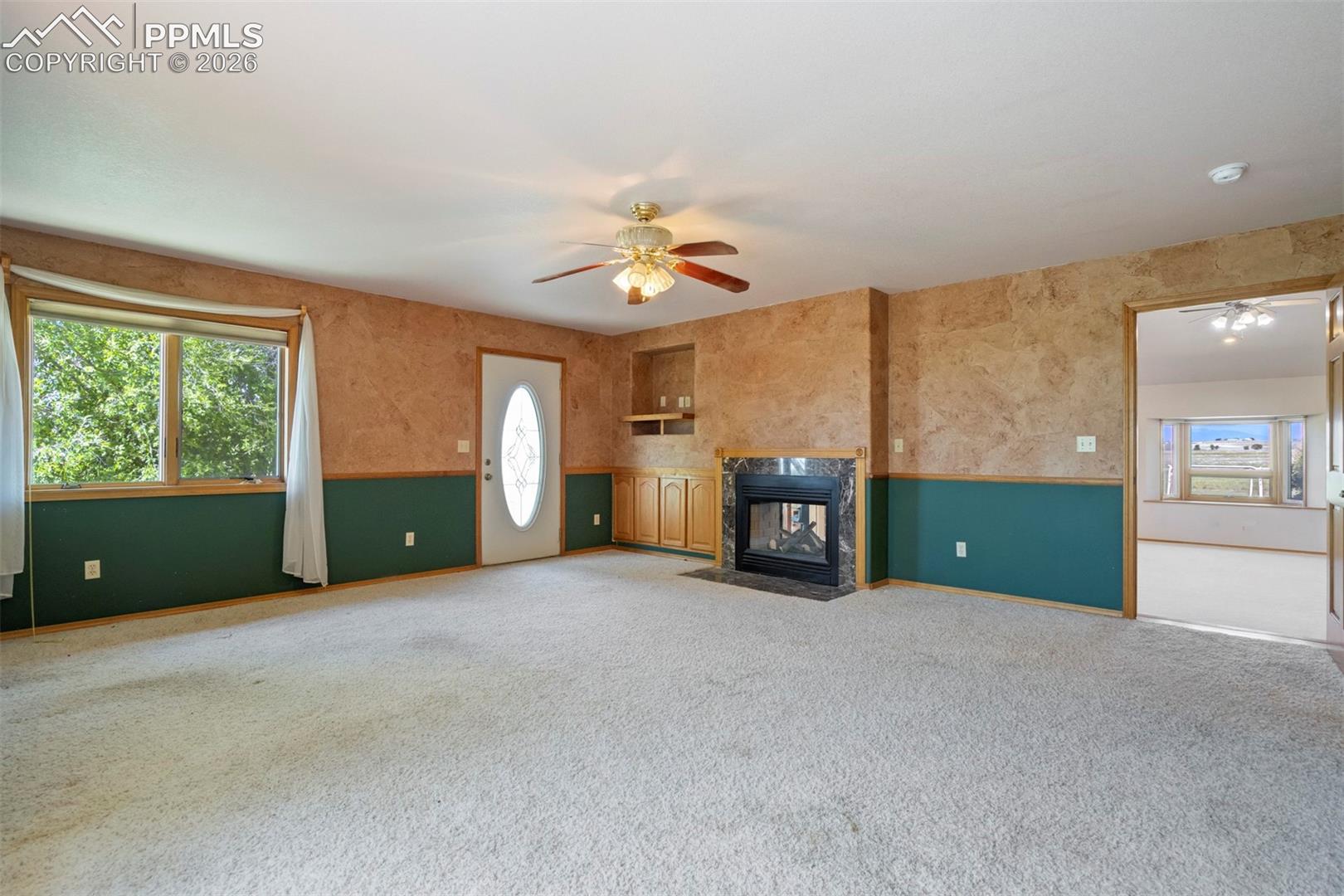 Spacious living area featuring light-colored carpeting and a ceiling fan