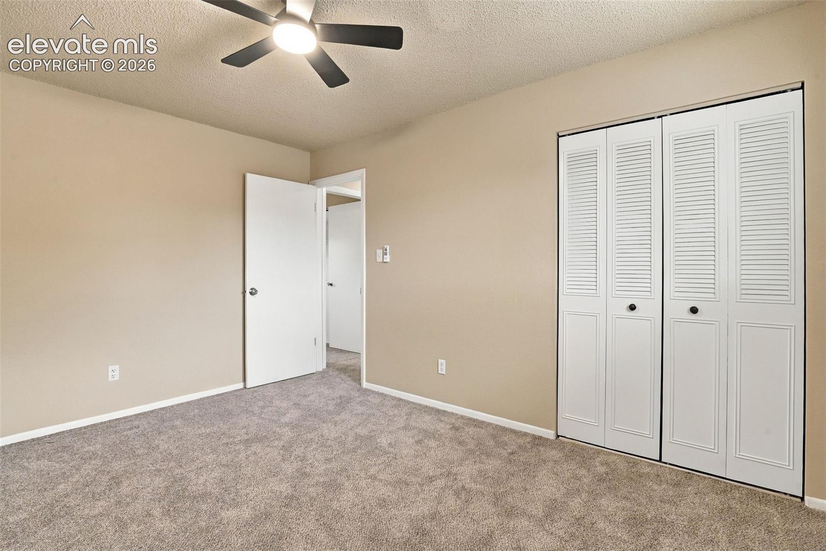 Neutral wall-to-wall carpeting, ceiling fan with integrated lighting, and white bifold closet doors with louvered detailing