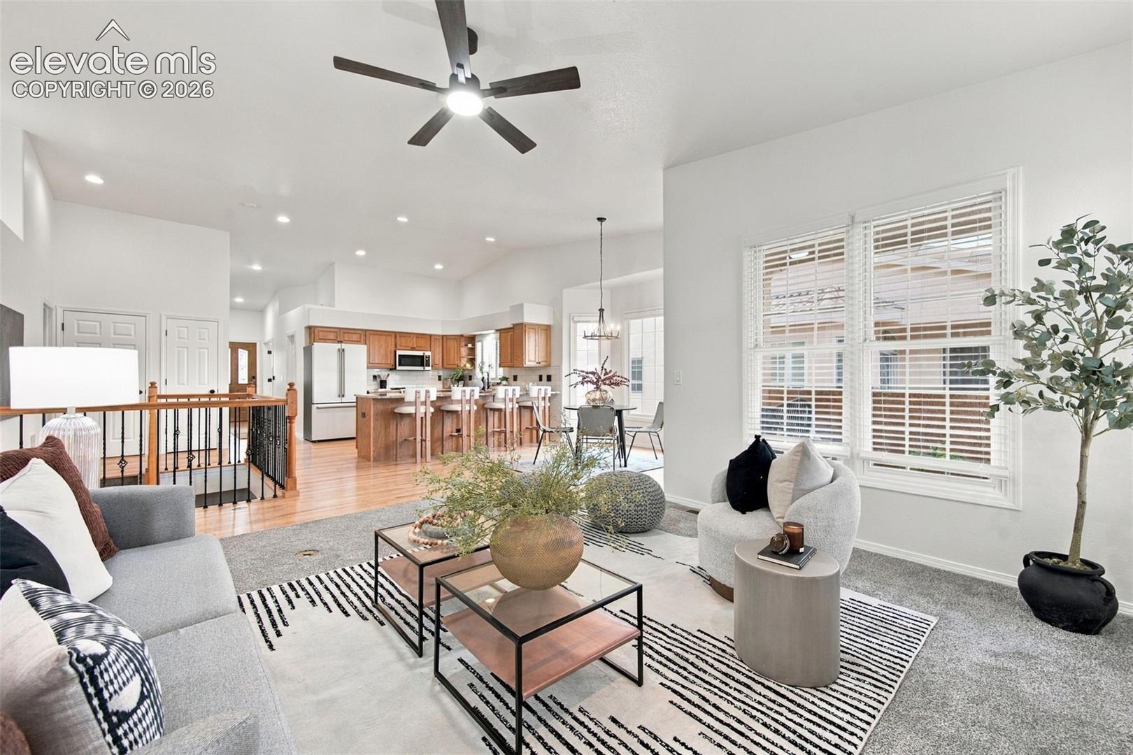 Open-concept interior featuring vaulted ceilings, recessed lighting, wood-finish cabinetry, a kitchen island with bar seating, and a decorative metal-spindle staircase railing
