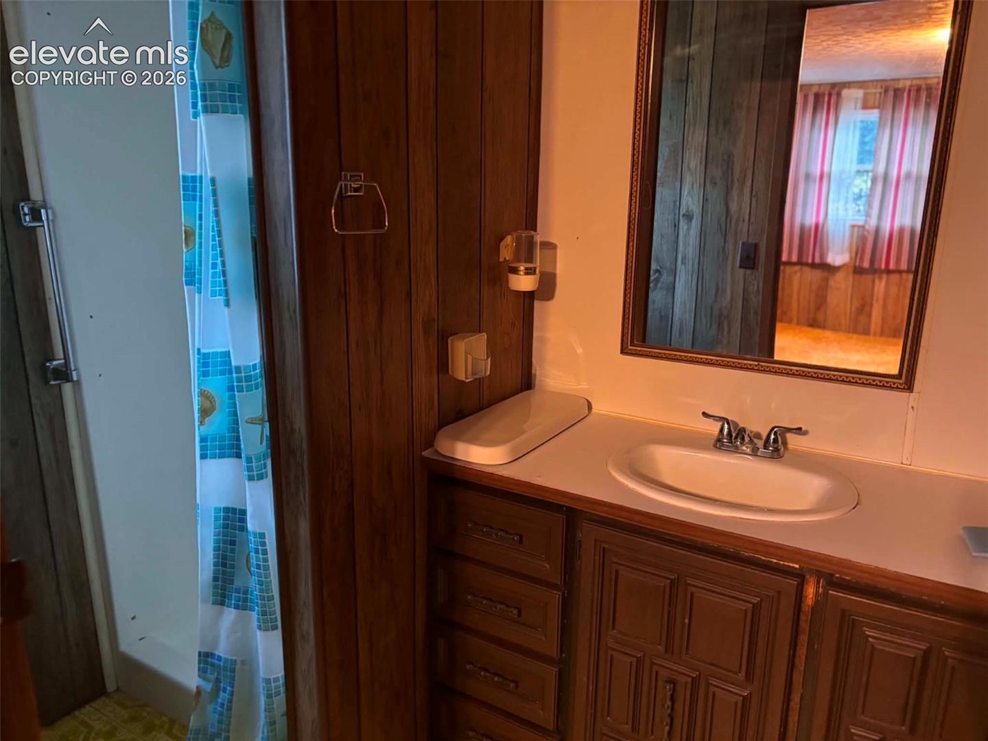 Bathroom featuring a wood-paneled vanity with integrated storage, an oval drop-in sink, a wall-mounted mirror with a decorative frame, and a shower enclosure