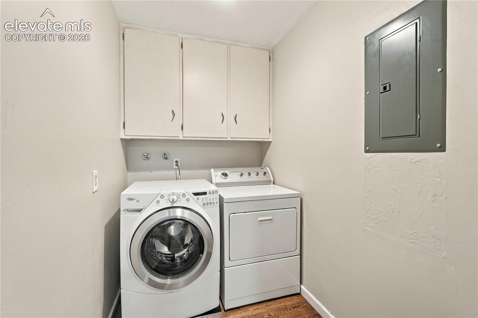 Utility space featuring built-in white cabinetry, washer, dryer, and an electrical service panel