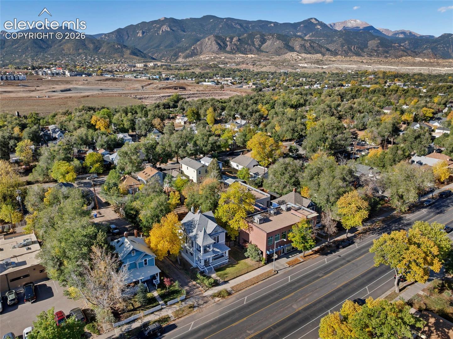 Aerial perspective showcasing a residential lot featuring mature trees, paved street access, and a prominent mountain range backdrop