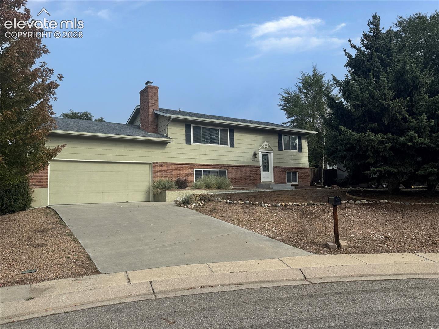 Split-level exterior featuring a brick and horizontal siding facade, attached two-car garage, brick chimney, and concrete driveway