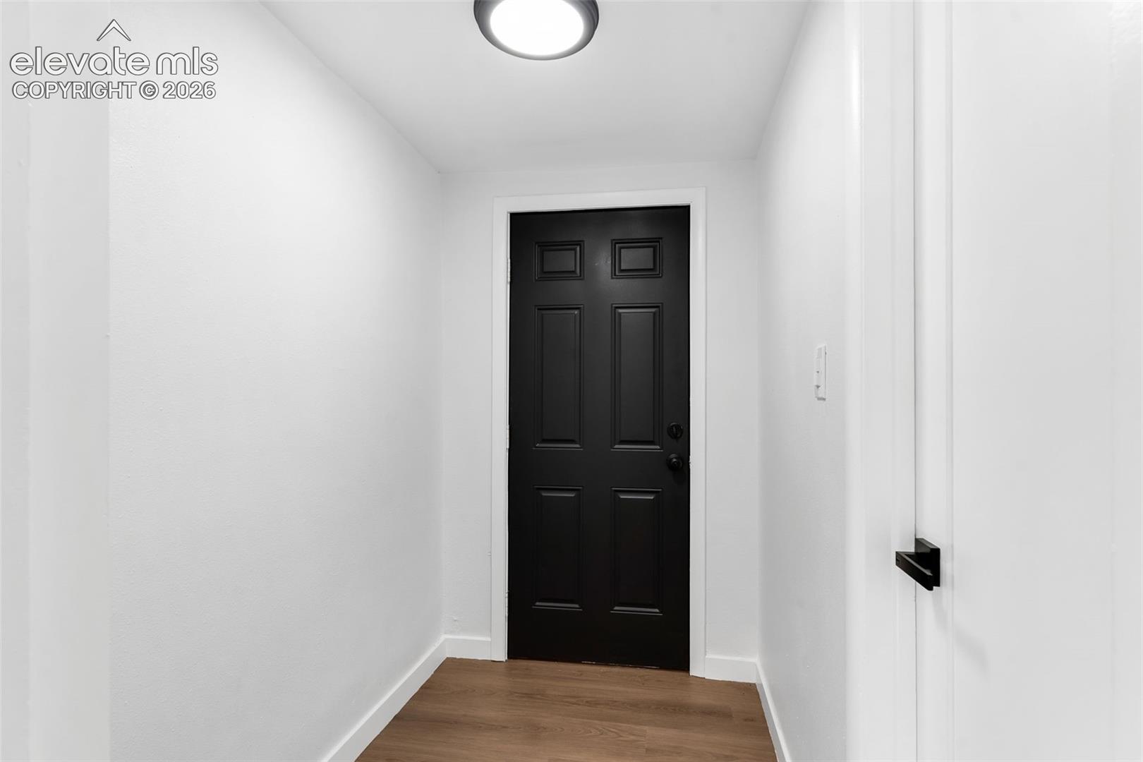 Interior entryway featuring a six-panel black door, white interior walls, wood-finish flooring, and a flush-mount circular ceiling light fixture
