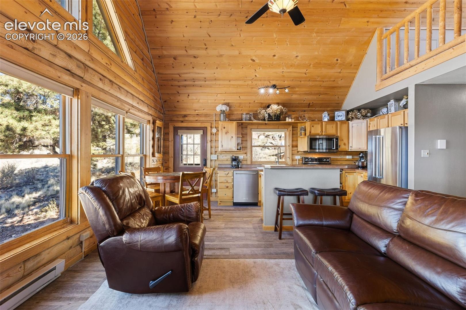 Vaulted ceilings with exposed wood beams, extensive natural log wall construction, multi-pane windows, stainless steel kitchen appliances, and a wooden loft railing