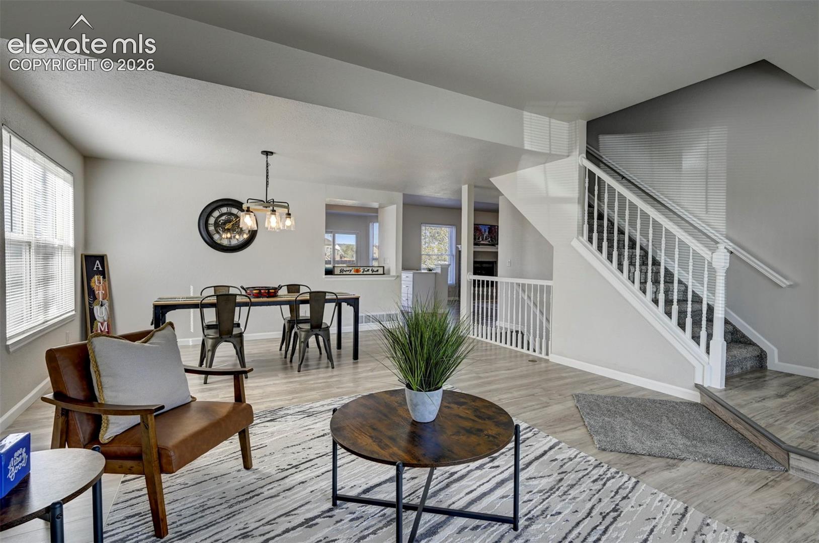 Neutral-toned interior featuring wood-finish flooring, staircase with white balusters, multi-light pendant fixture, and a wall cutout providing a sightline into another space