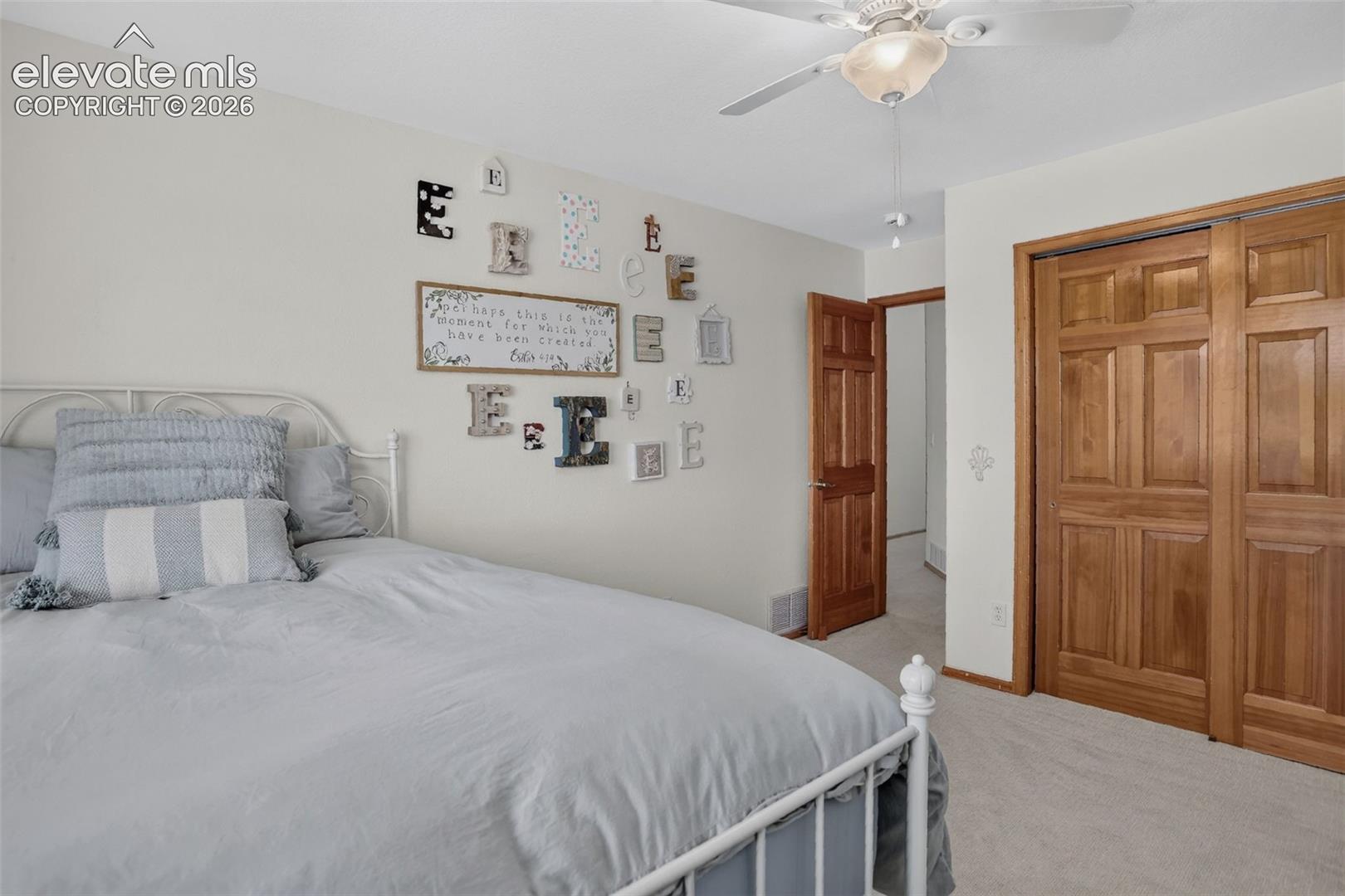 Bedroom featuring light wall color, a ceiling fan with integrated lighting, wood-finish doors, paneled closet doors, and light-colored carpeting