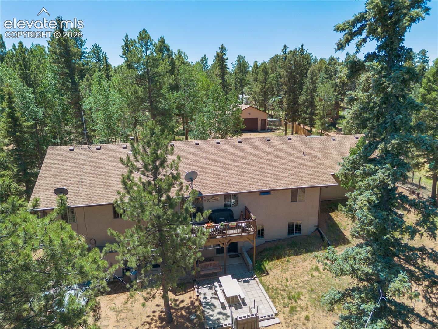 Exterior featuring a multi-level structure with a brown shingle roof, a wood deck, and a ground-level patio