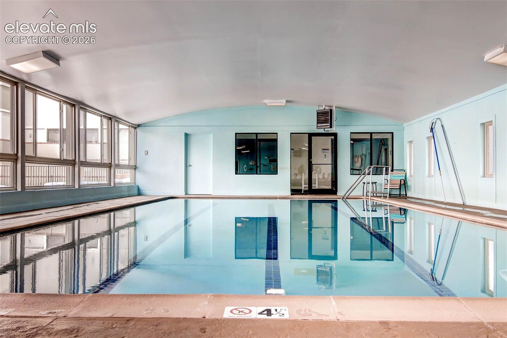 Indoor swimming pool featuring a curved ceiling, full-height windows, a glass-paneled entry door, and light blue wall accents