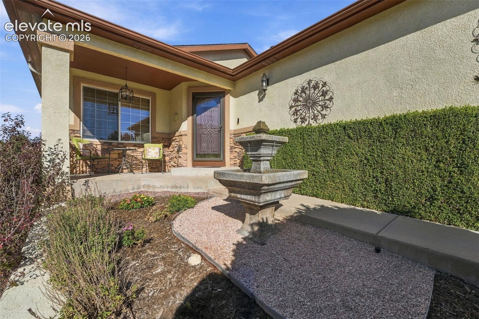 Stucco exterior featuring stacked stone accents, covered entryway, tiered concrete fountain, and low-maintenance landscape beds