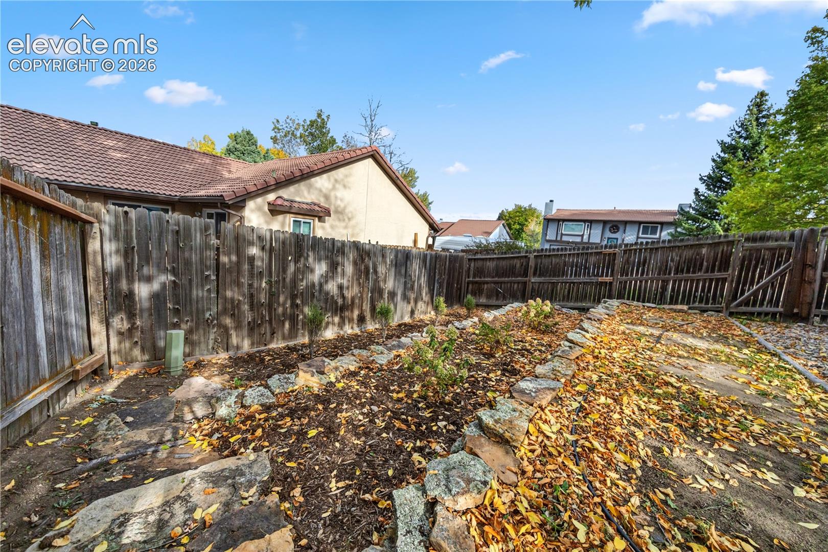 Backyard featuring a tiered stone retaining wall, natural wood fencing, and mulched landscaping beds